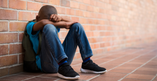 Young boy with head in arms leaning against wall