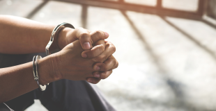 Hands in handcuffs clasped in front of bars