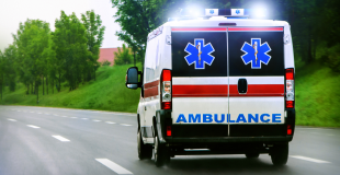 An ambulance with lights on driving on a road