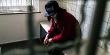 A teen sits in a cell looking down