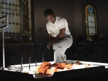 A man in a prison uniform kneels during a performance onstage